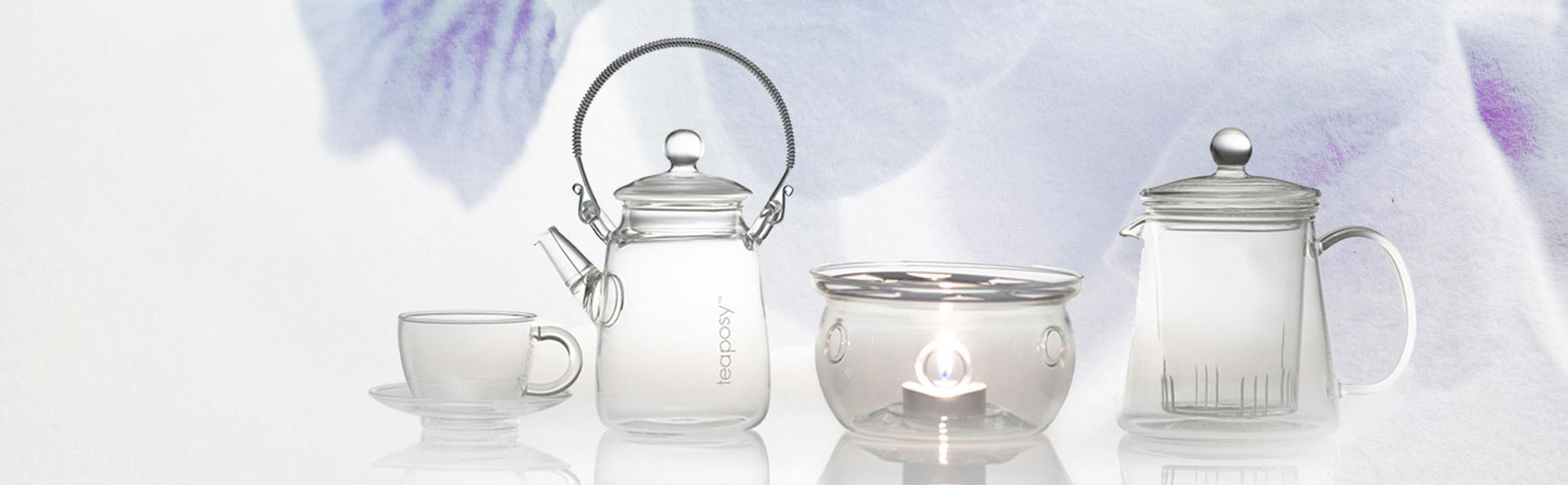 A collection of four glass teawares including two teapots one cup and saucer set, and a tea warmer